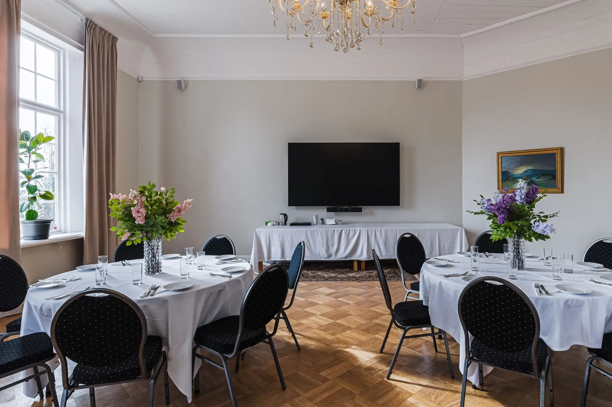 Ein heller Festsaal mit rund eingedeckten Tischen.
