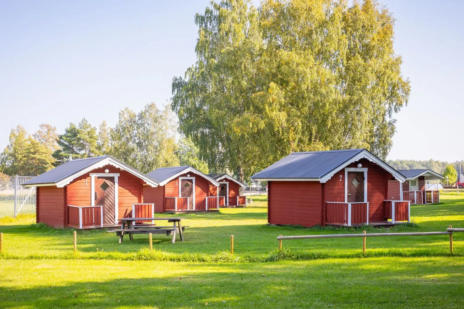 Små röda stugor vid vattnet omgivna av skog.