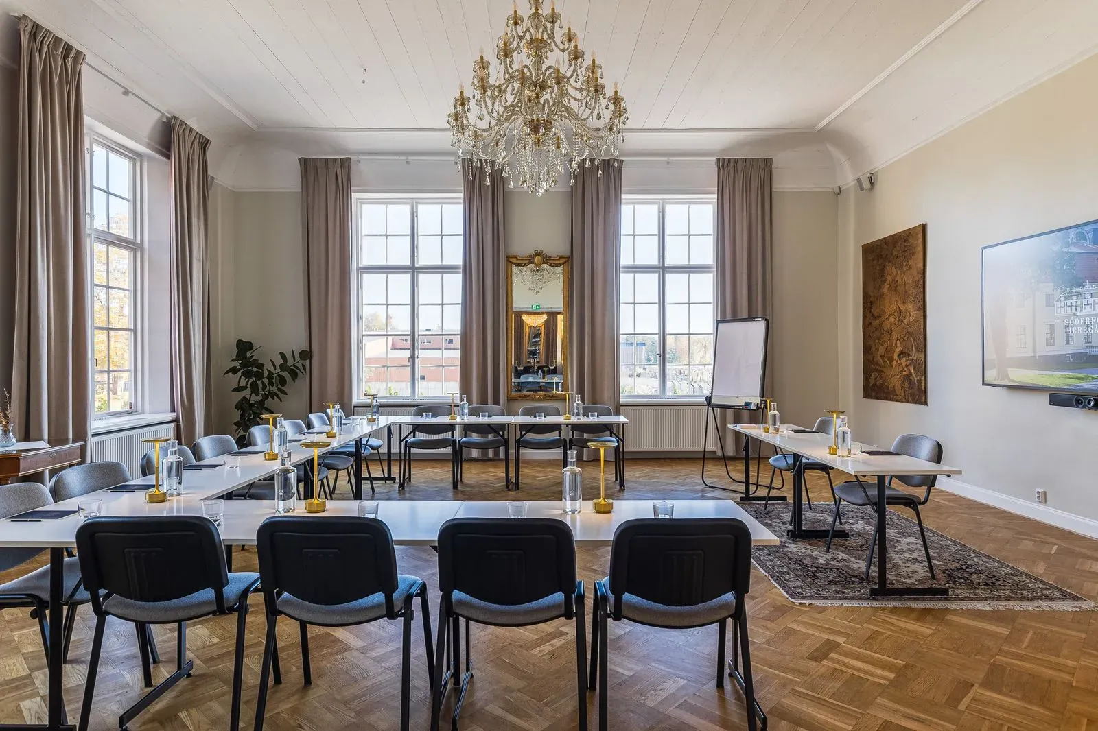 Ljust konferensrum med bord i U-sittning, stora fönster och kristallkrona.