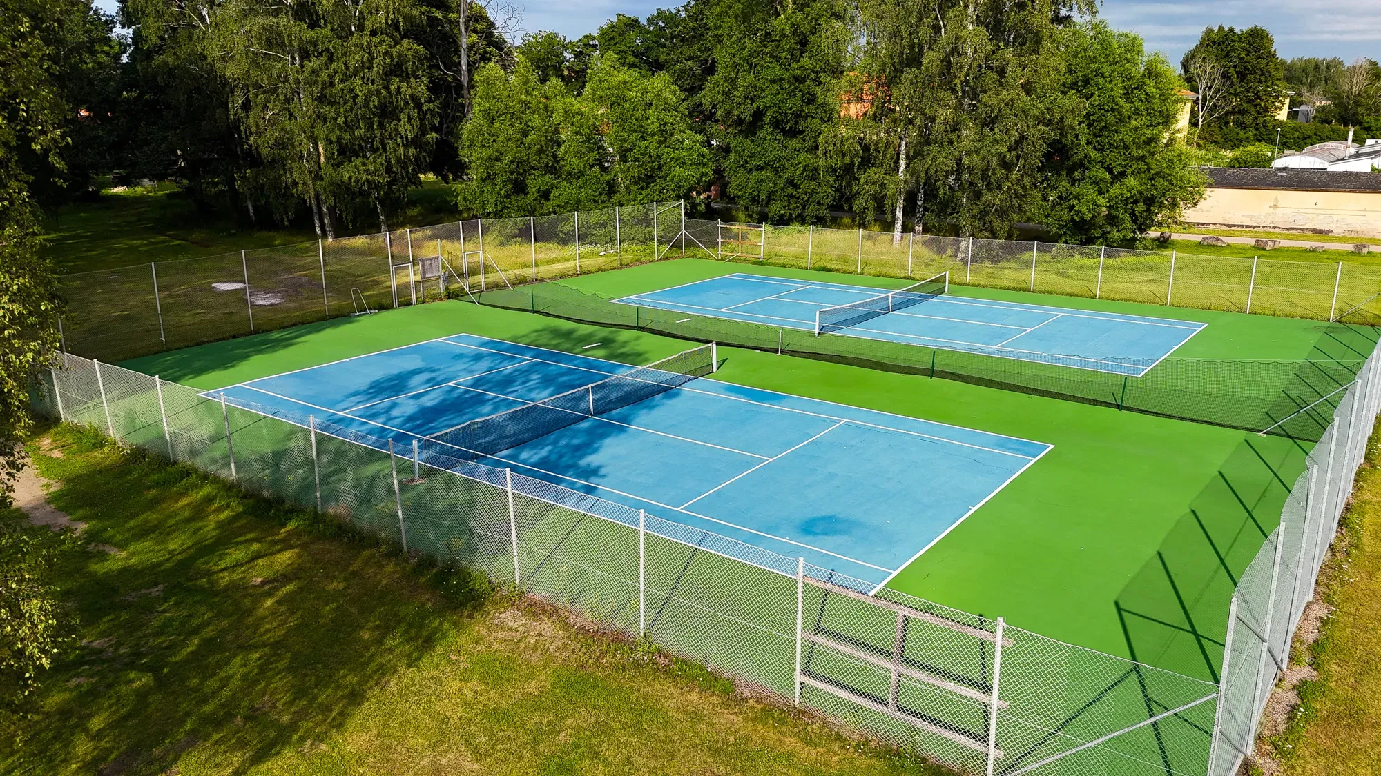 Zwei von Grün umgebene Tennisplätze.