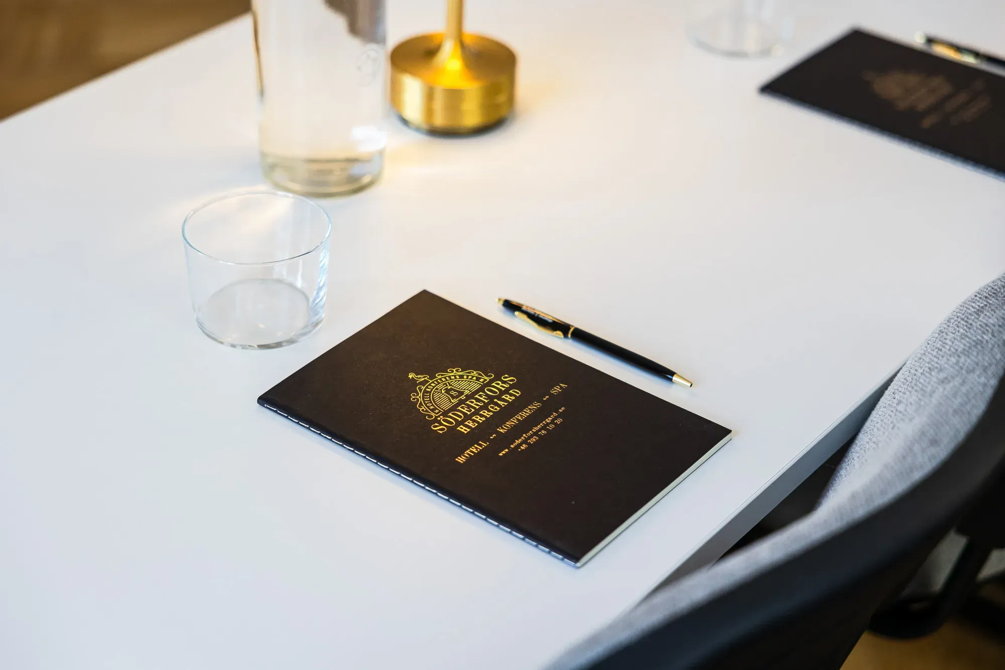 Notizbuch, Stift, Wasser und Tagungsleuchte auf einem vorbereiteten Tisch.