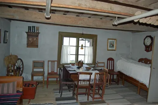 Historisk interiör i Gammelgården med matbord, stolar och äldre bruksföremål.