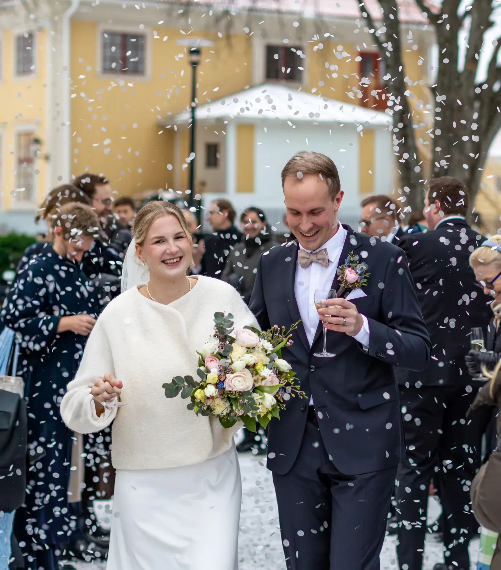 Ein Hochzeitspaar und Gäste feiern mit Konfetti vor dem Herrenhaus.